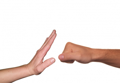 Na zdjęciu widzimy dwie dłonie skierowane ku sobie, jedna złożona jest w pięść symbolizującą agrsję i przemoc, druga jest rozłożona, palce wyprostowane, w stylu blokady - symbol zatrzymania agresji i przemocy.